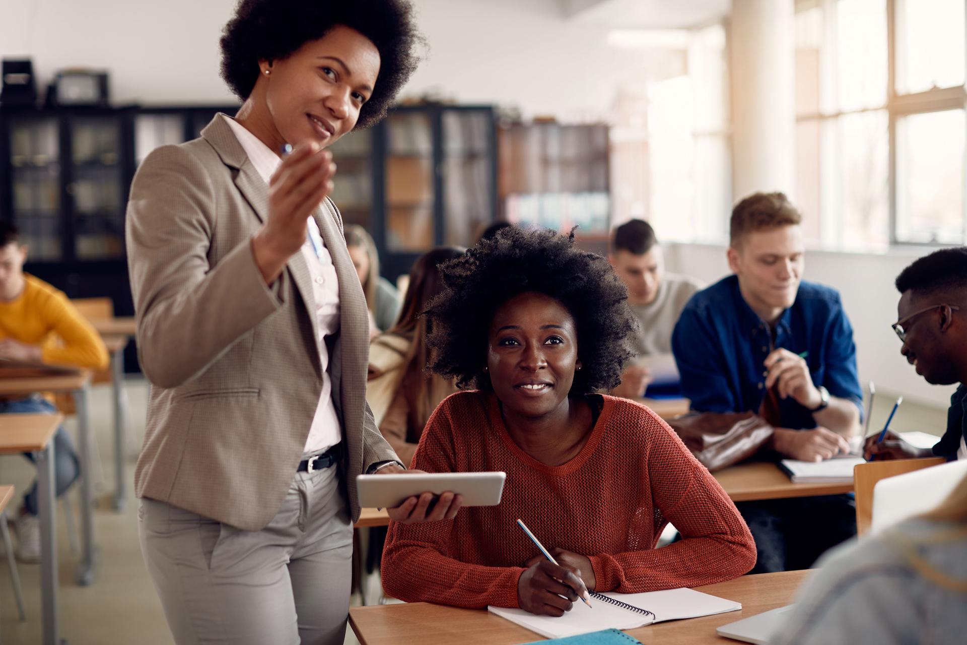 African American professor using touchpad while assisting her student on a class at the university.